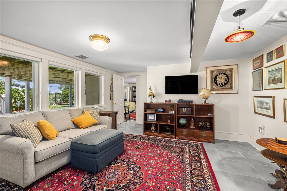 Living room with a gray sectional, red patterned rug, and wooden shelves beneath a wall-mounted television.