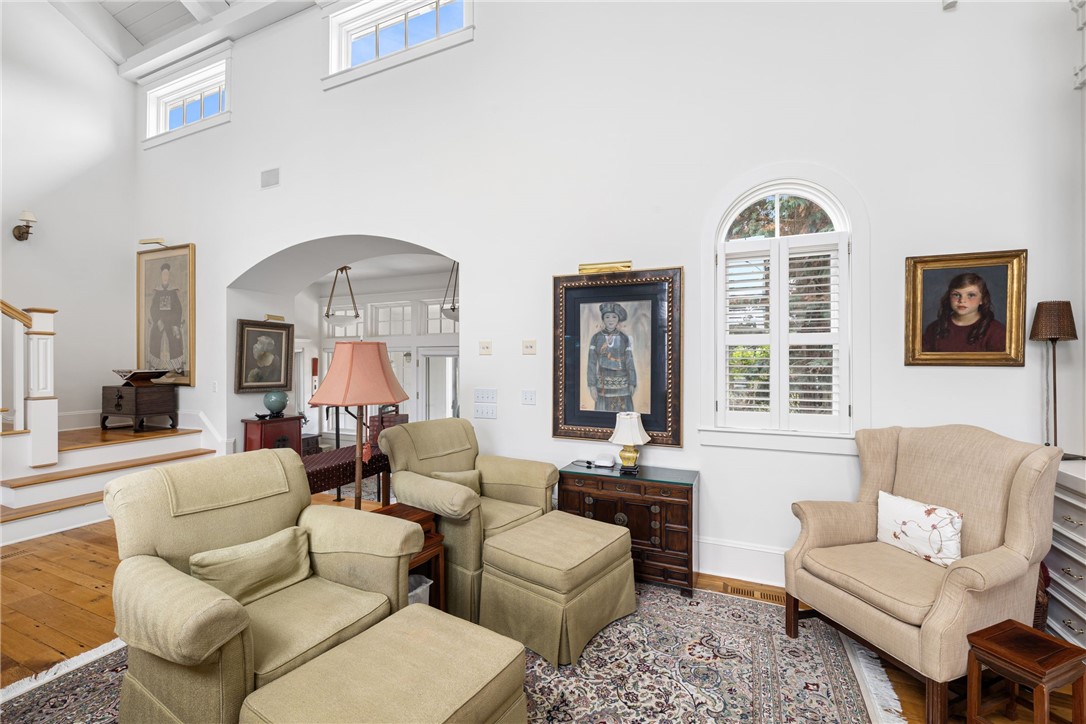 Living room with a vaulted ceiling, arched shuttered window, cream seating, patterned rug, and wood floors.