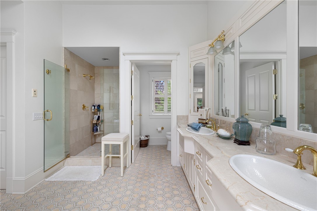 Bright bathroom with a glass shower, double vanity, large mirrors, and patterned tile floor.