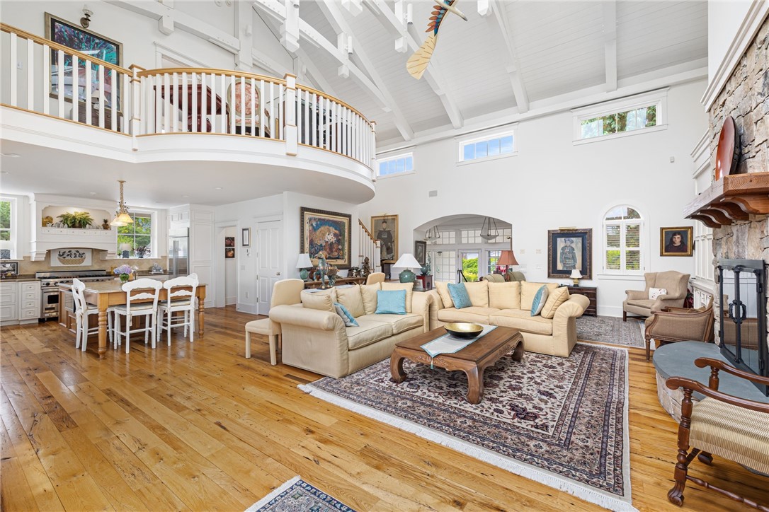 Double-height living room with loft railing, exposed beams, and adjoining kitchen.