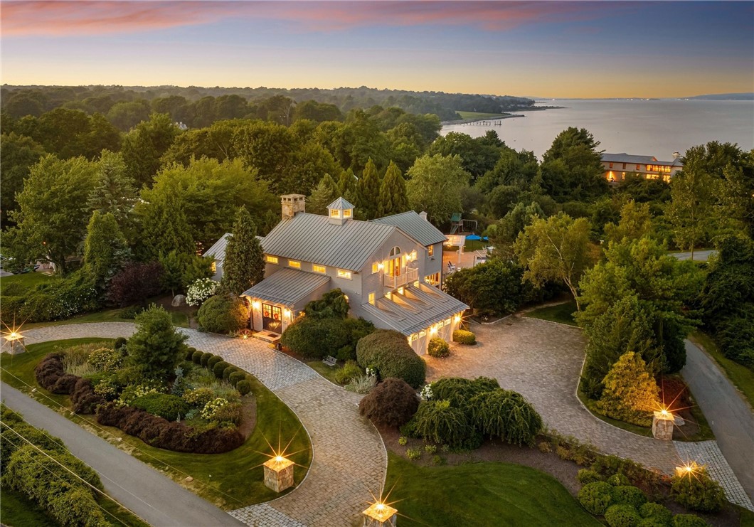 Aerial view of a gray-roofed home with landscaped grounds and the bay beyond.