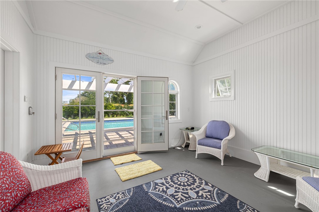 Sunroom with wicker seating and glass doors overlooking a patio and swimming pool.