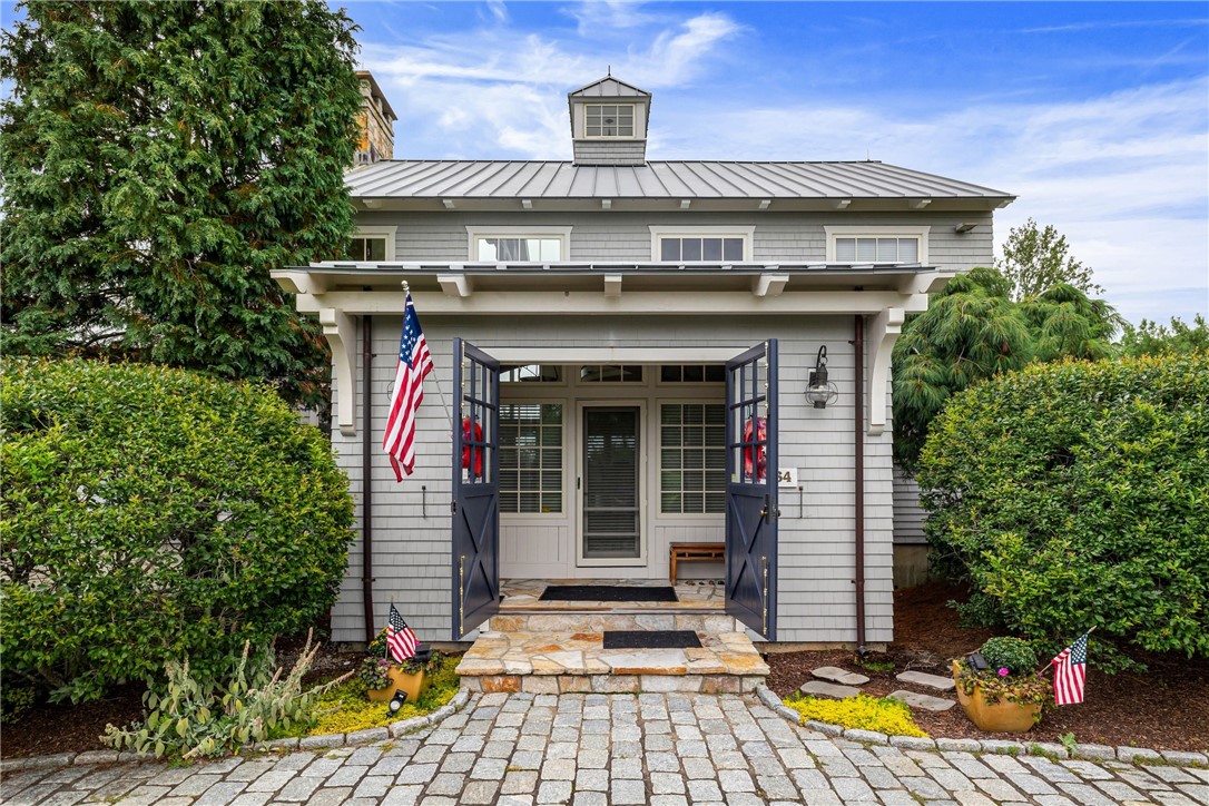 Gray shingle-sided home with open navy entry gates, stone steps, and a cobblestone walkway.