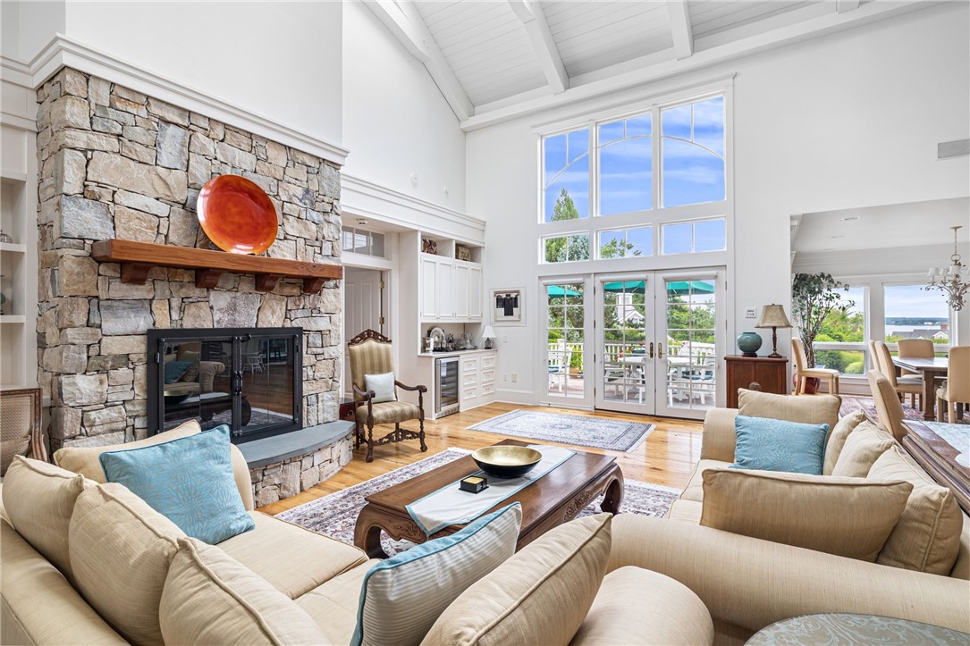 Living room with a stone fireplace, vaulted ceiling, and distant water views through large windows.