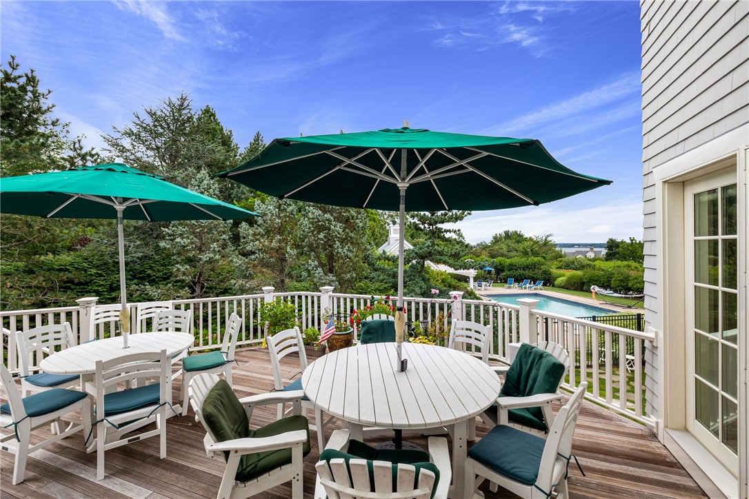 Furnished deck with green umbrellas and white seating overlooking a backyard swimming pool.