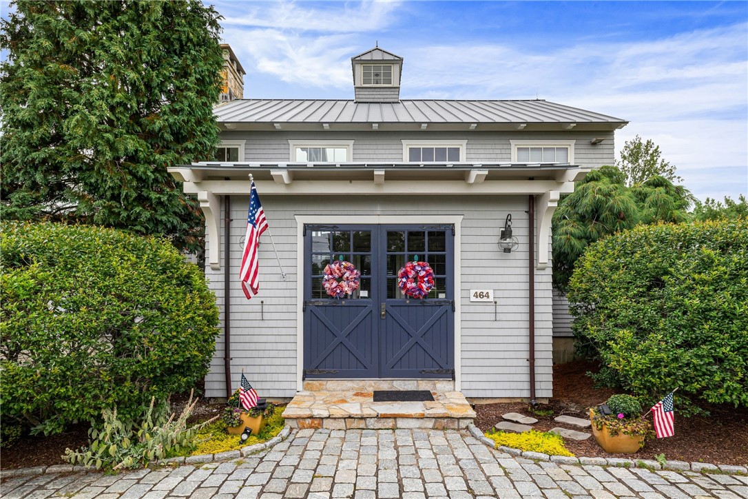 Gray shingle home with blue crossbuck entrance doors, stone walkway, and American flags.
