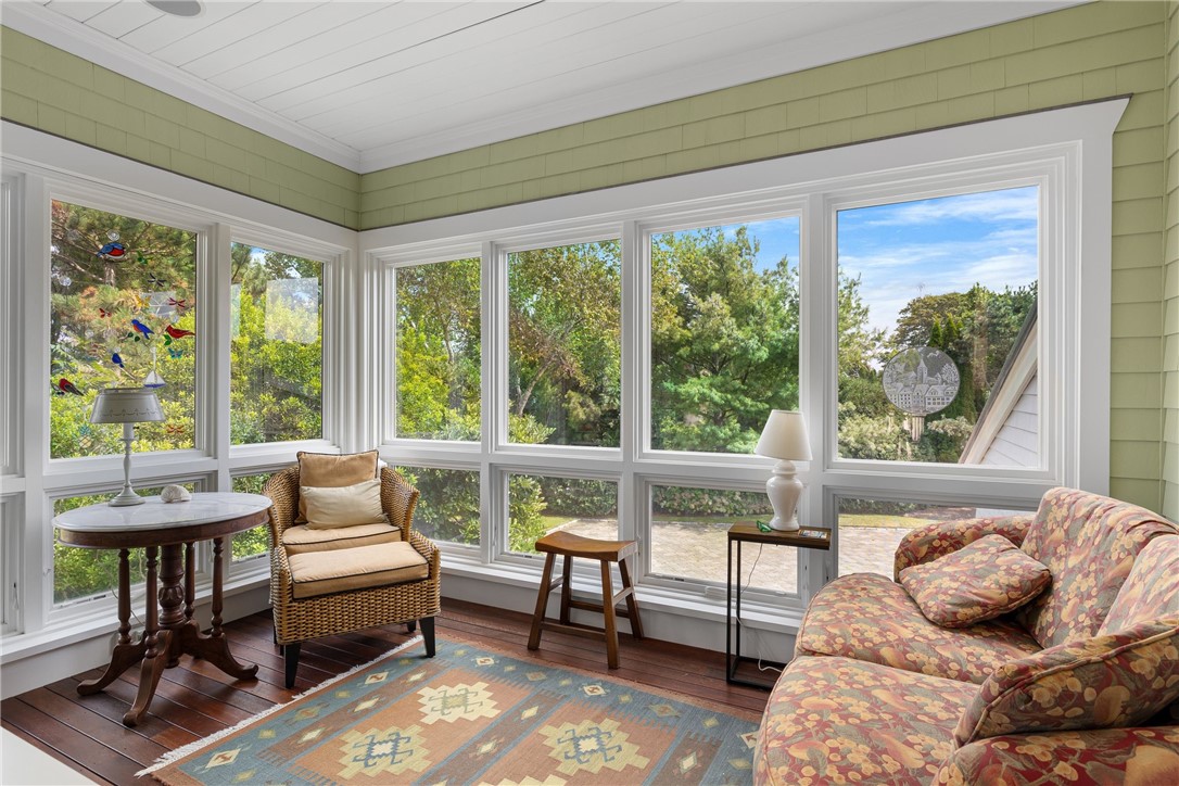 Furnished sunroom with expansive windows, a wicker chair, floral sofa, and leafy garden views.