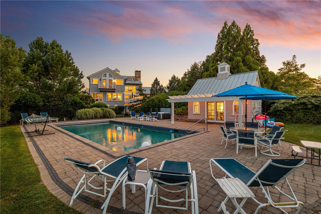 Backyard pool and patio beside a gray home at dusk.