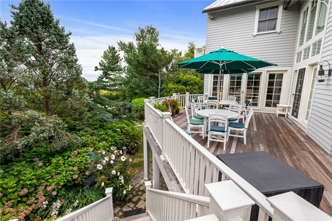 Wood deck with outdoor dining beneath a teal umbrella, overlooking lush gardens beside the home.