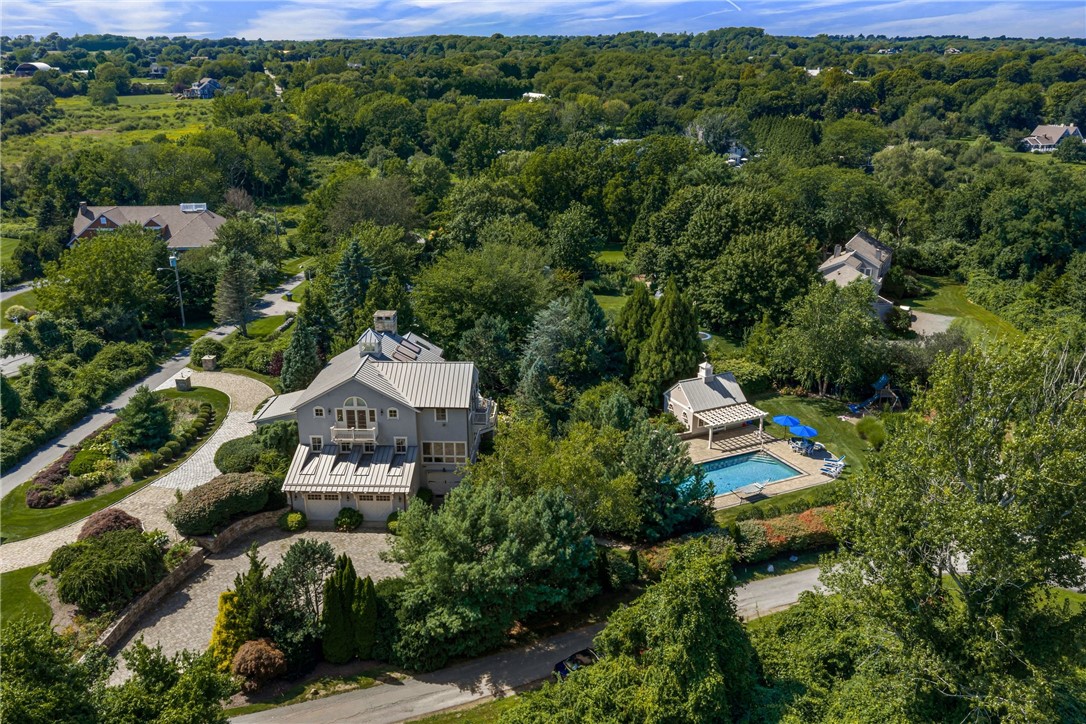 Aerial view of a gray home with a swimming pool, pool house, and landscaped grounds.