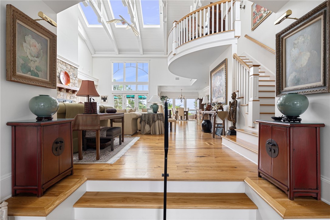 Open living room with vaulted skylit ceiling, hardwood floors, and a sweeping staircase.