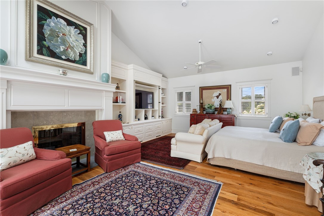 Bedroom with fireplace, built-in cabinetry, red chairs, and a large bed.