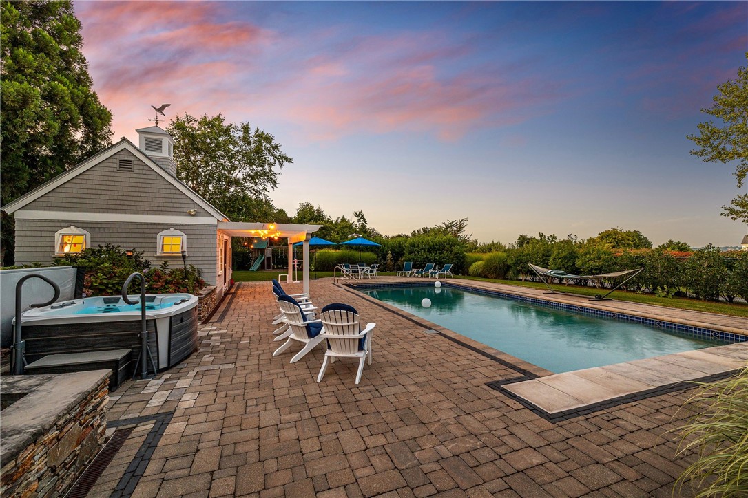 Home with a swimming pool and hot tub on a broad paved patio at dusk.