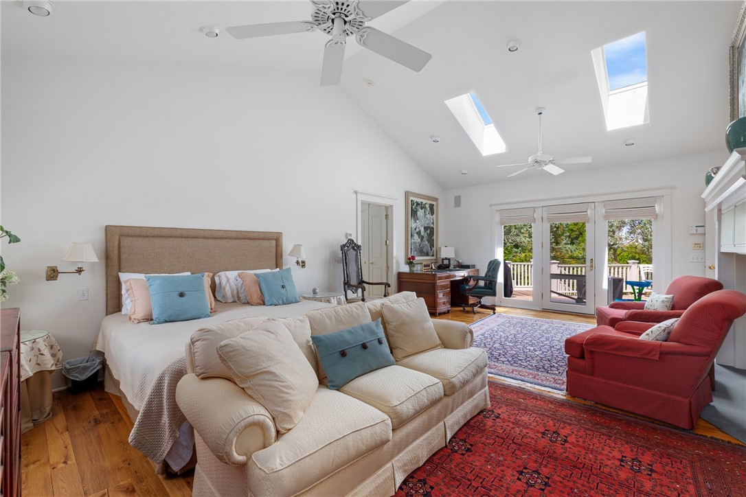 Furnished bedroom with a sitting area, vaulted ceiling, skylights, and French doors to a deck.