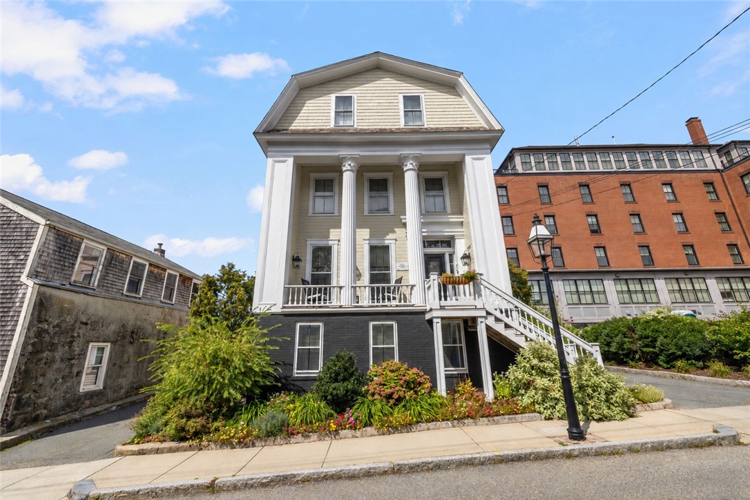 Columned three-story home with a white porch railing and landscaped flower beds.