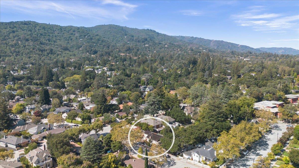 Aerial neighborhood view with a white circle highlighting a home beneath wooded hills.
