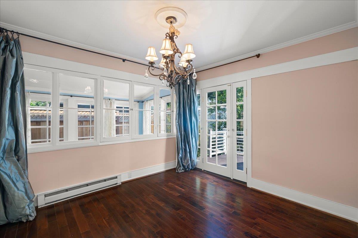 Vacant room with pink walls, dark hardwood floors, a chandelier, and French doors opening to a deck.