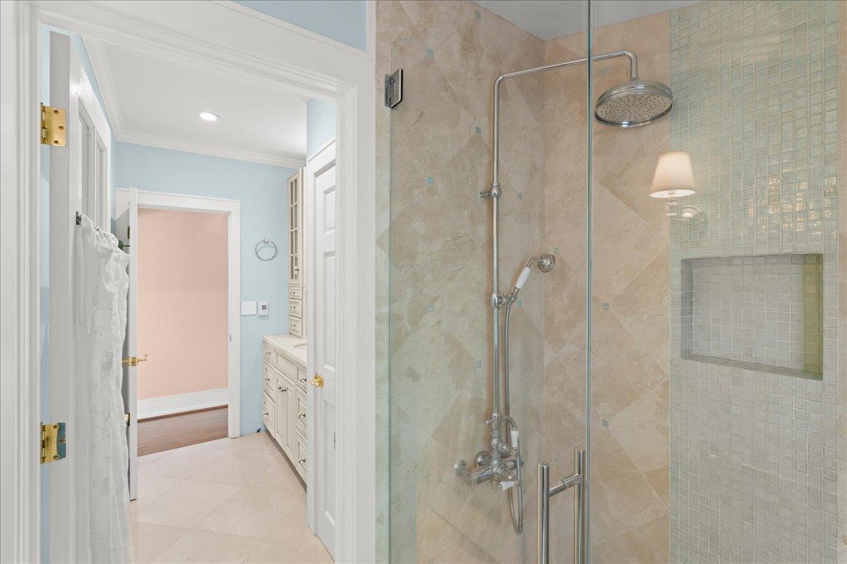 Bathroom with a glass-enclosed stone-tile shower and inset mosaic niche beside a white vanity.