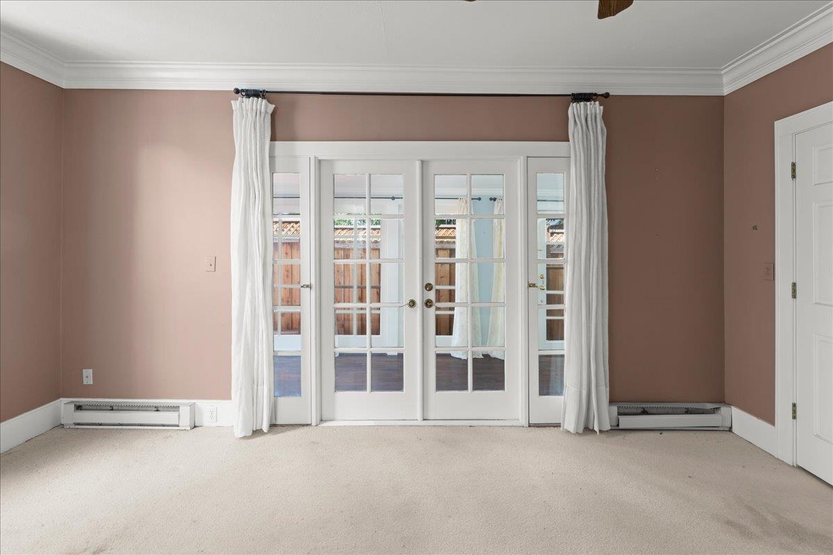 Empty carpeted room with French doors, white curtains, and muted rose-brown walls.