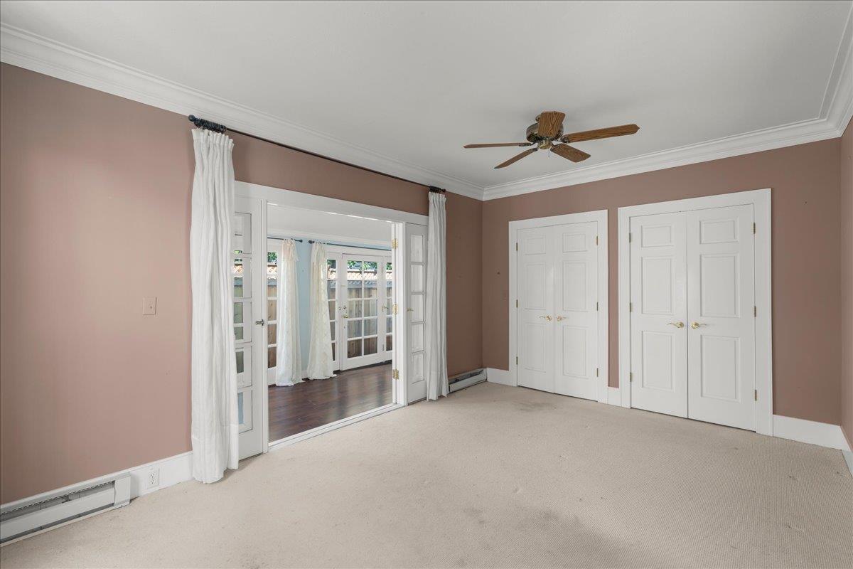 Empty bedroom with beige carpet, double closet doors, and open French doors to a wood-floored room.
