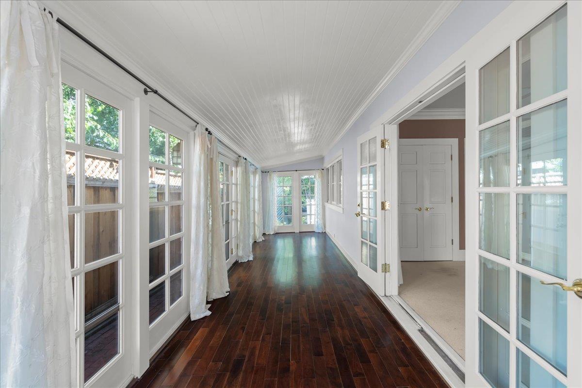 Empty sunroom with dark hardwood floors, a white beadboard ceiling, and tall French windows.