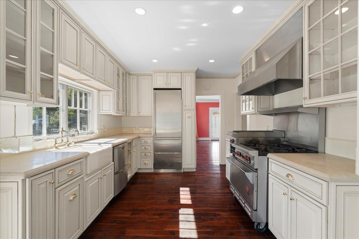 Kitchen with cream cabinetry, glass-front cupboards, stainless-steel appliances, and dark hardwood floors.
