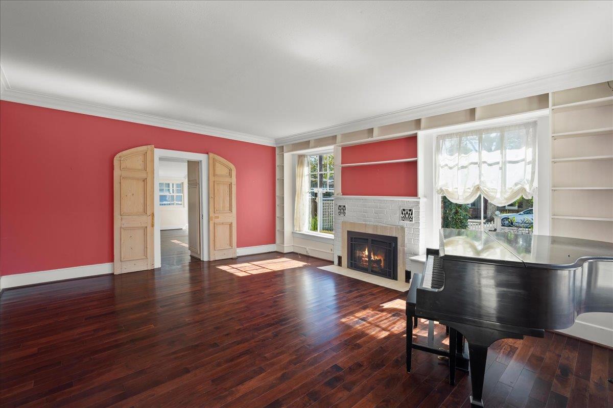 Living room with a grand piano, red walls, built-in shelves, and a white brick fireplace.