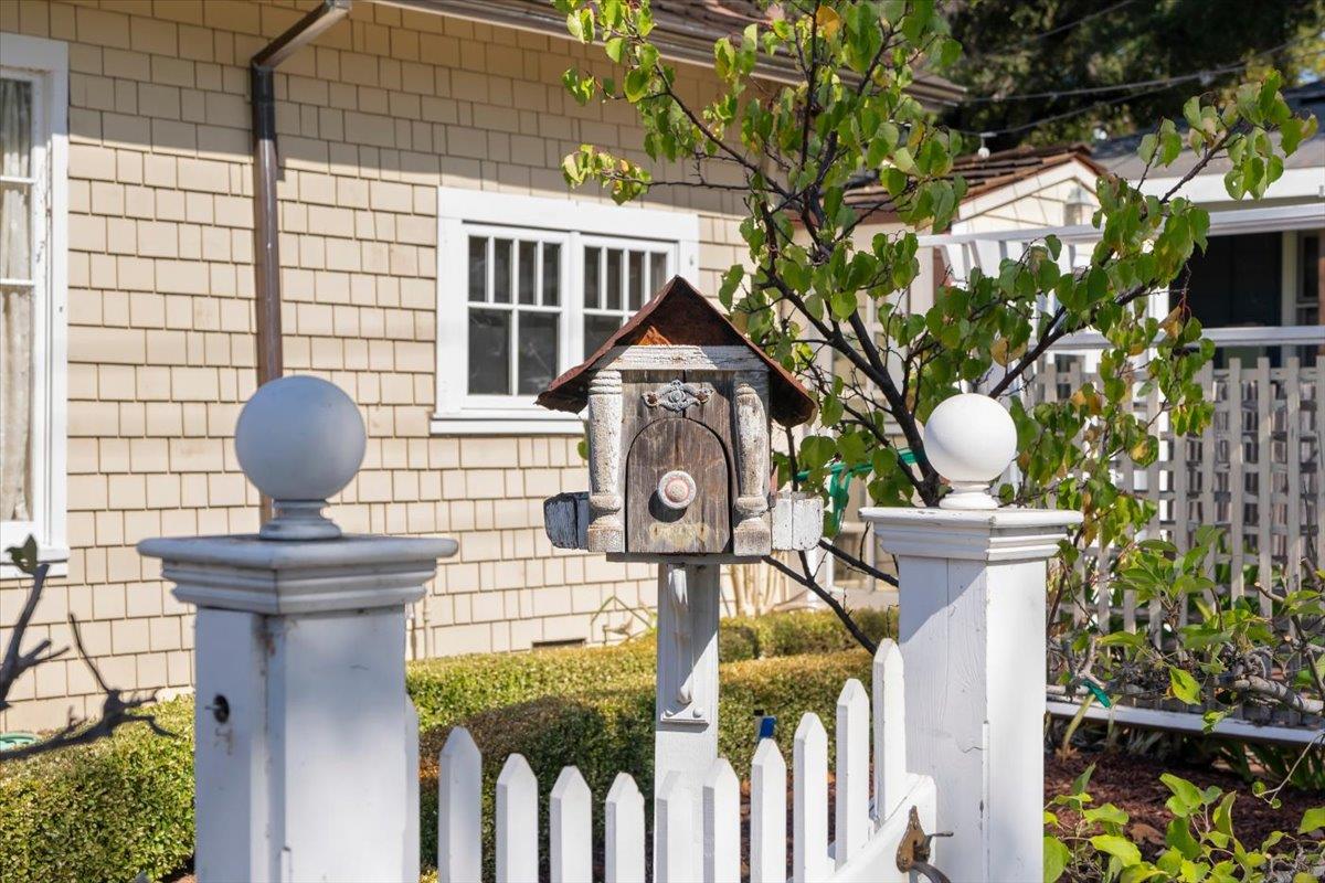 Wooden mailbox stands between white fence posts in front of a shingled home.