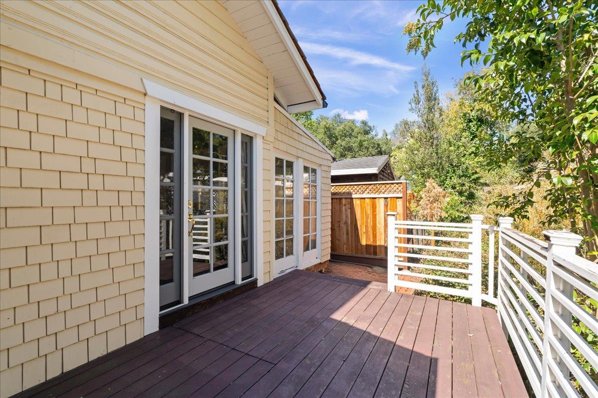 Raised wooden deck beside a cream shingle-sided house, with white railings and glass doors.