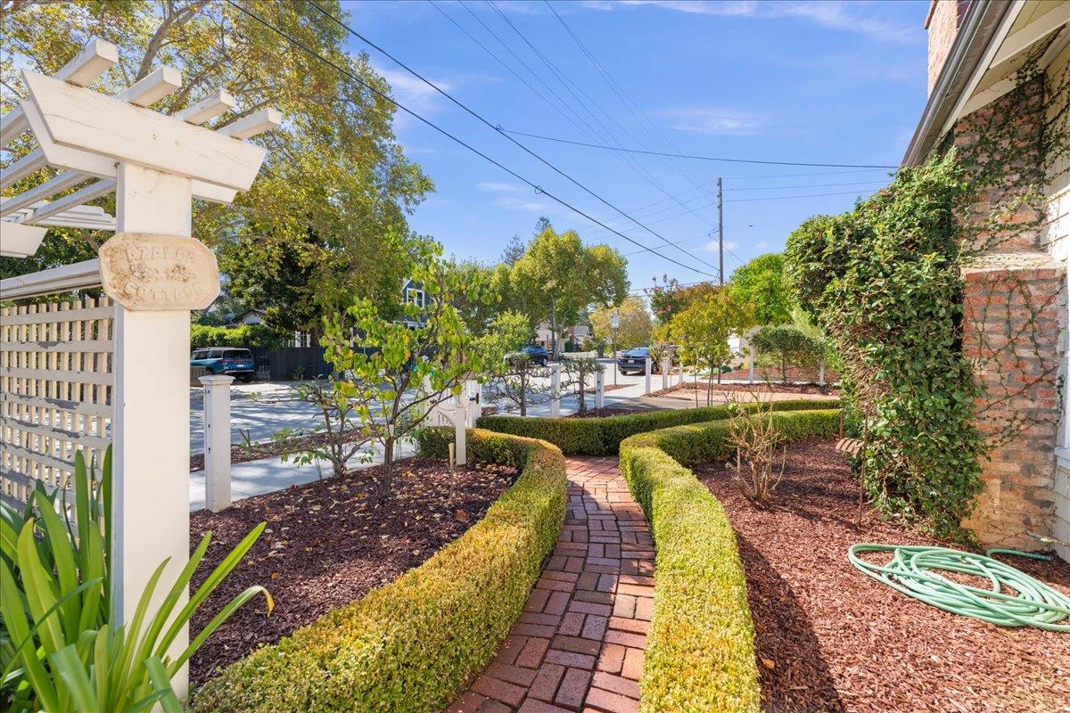 Landscaped front entry with a brick path, clipped hedges, and white pergola.