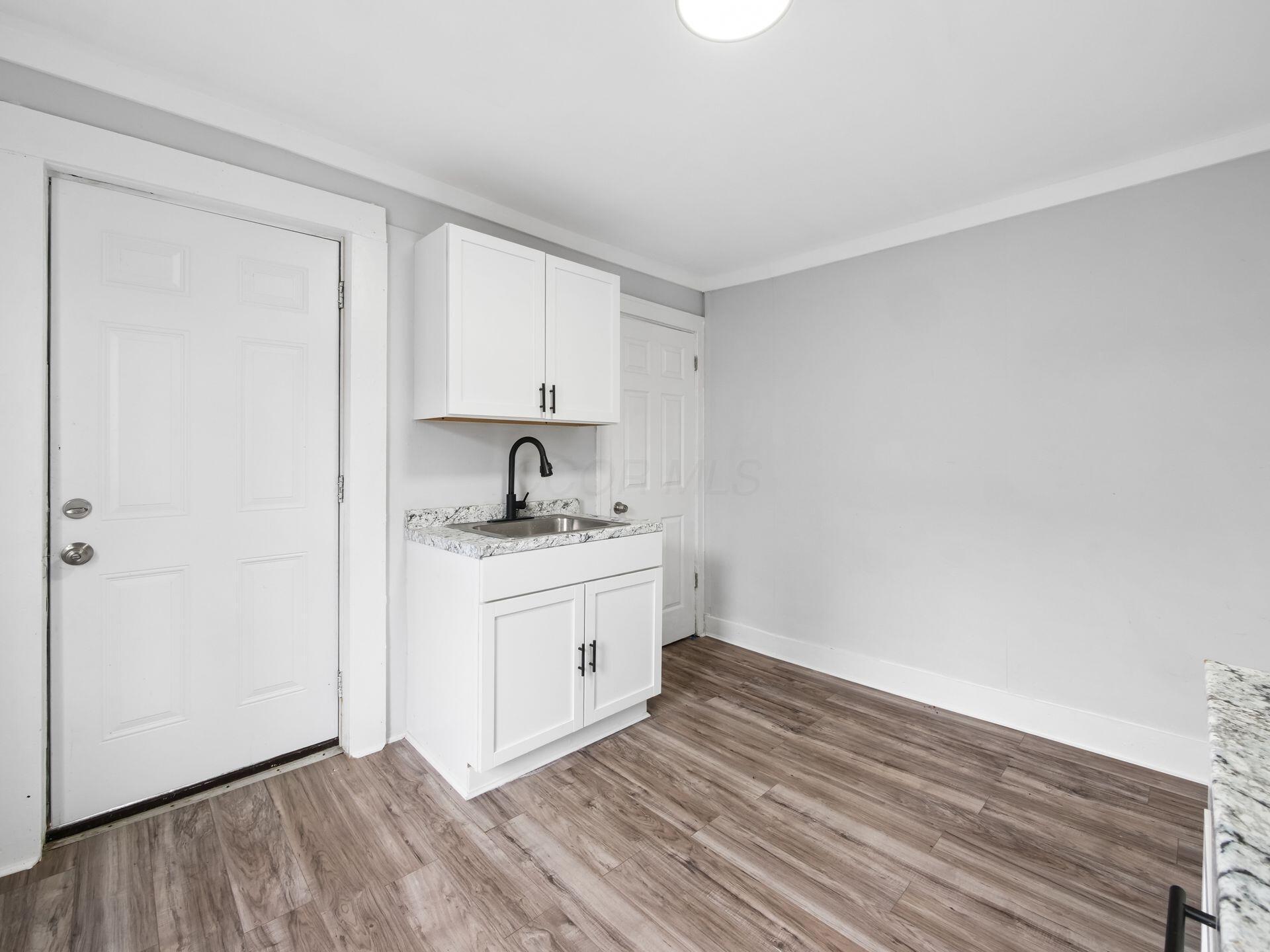Compact kitchen with white cabinets, stainless steel sink, black faucet, and wood-look flooring.