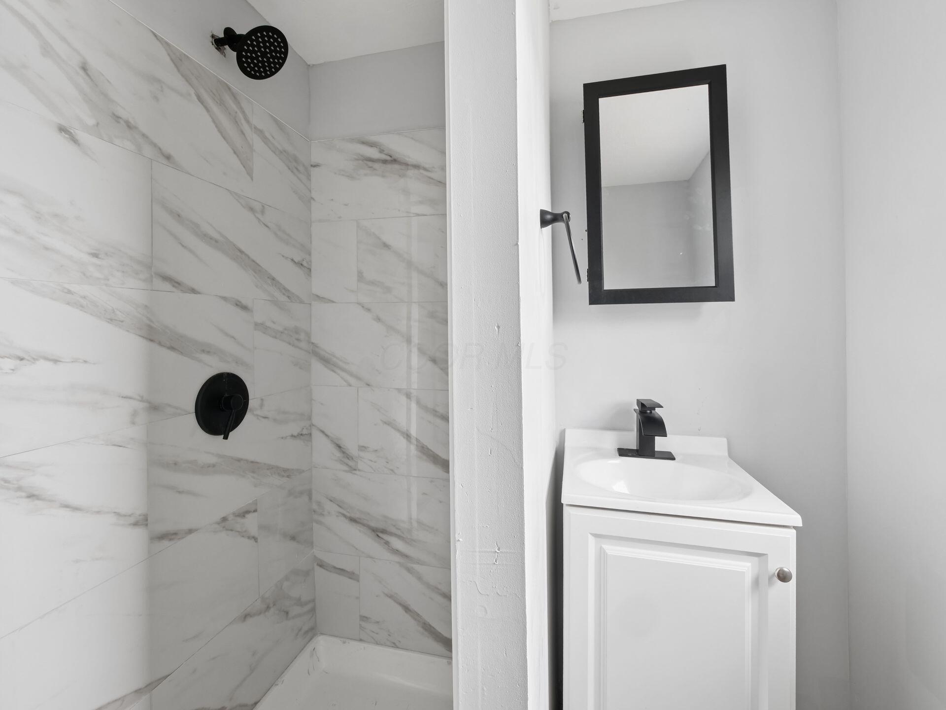 Bathroom with a marble-look tiled shower, black fixtures, and a white vanity.