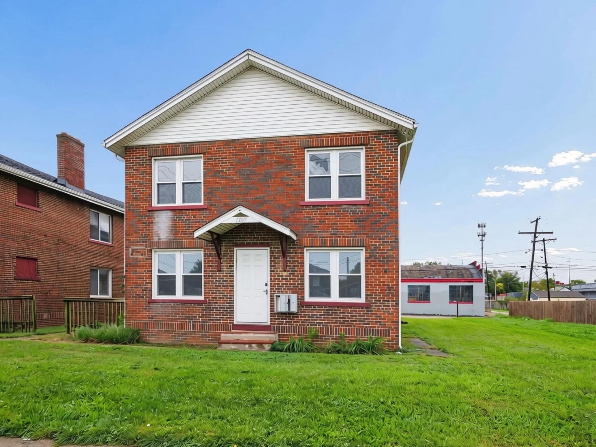 Two-story red brick house with white gable siding, a covered entry, and a broad green lawn.