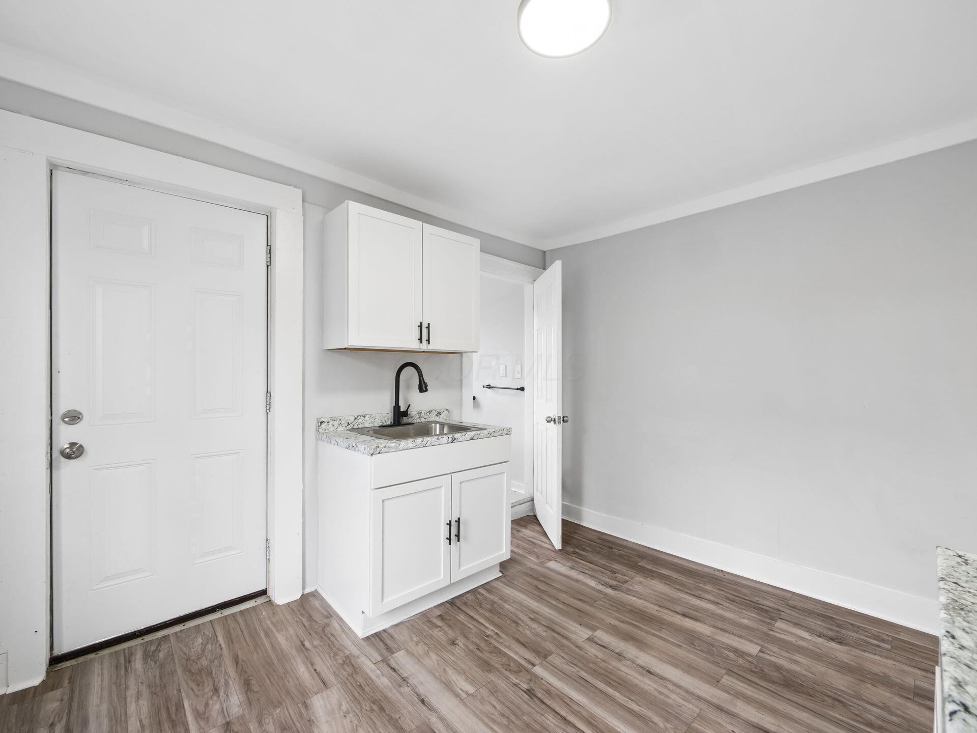 Small empty room with a white sink cabinet, black faucet, and wood-look flooring.