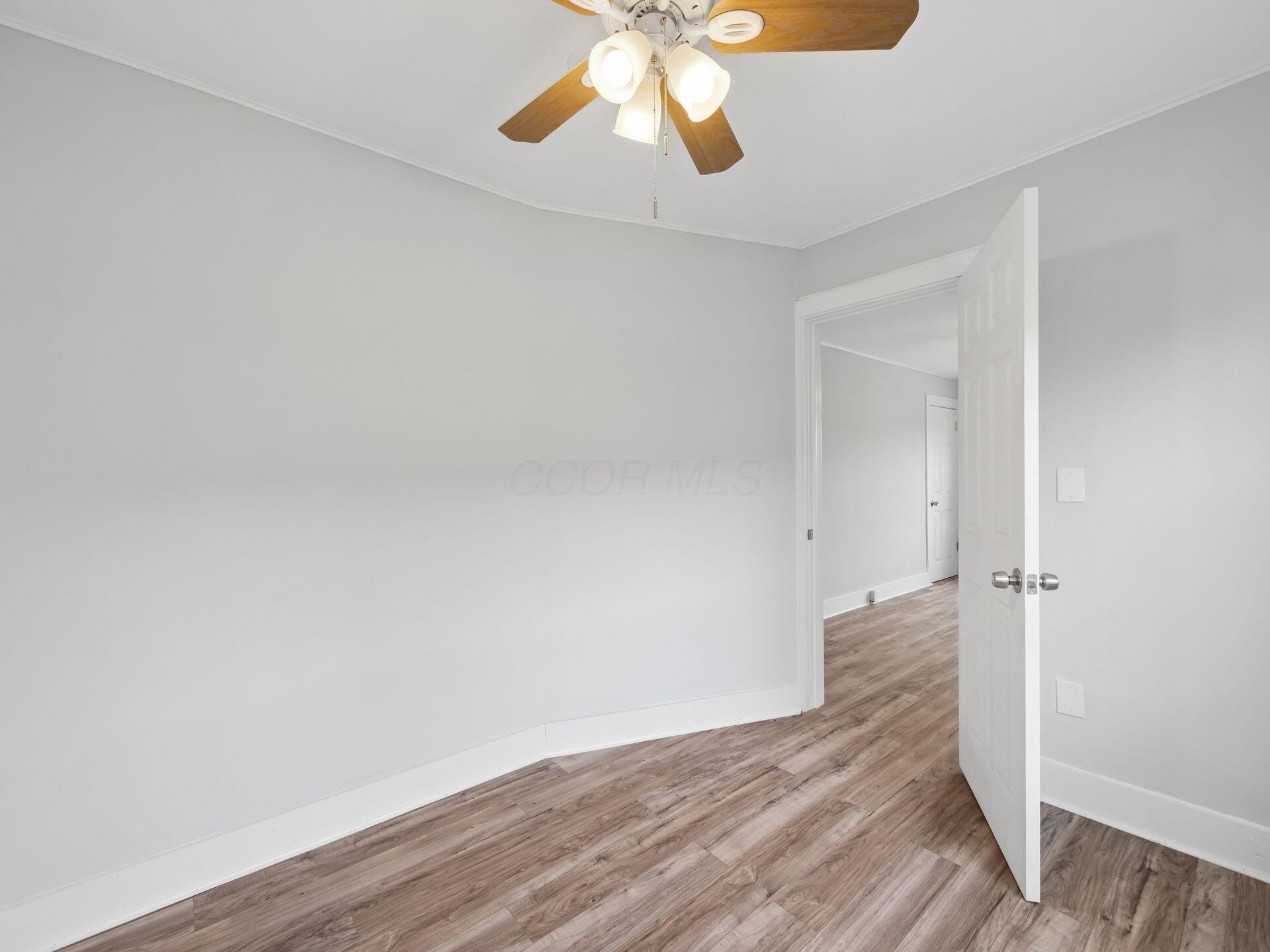 Empty room with wood-look flooring, gray walls, and a ceiling fan beside an open doorway.
