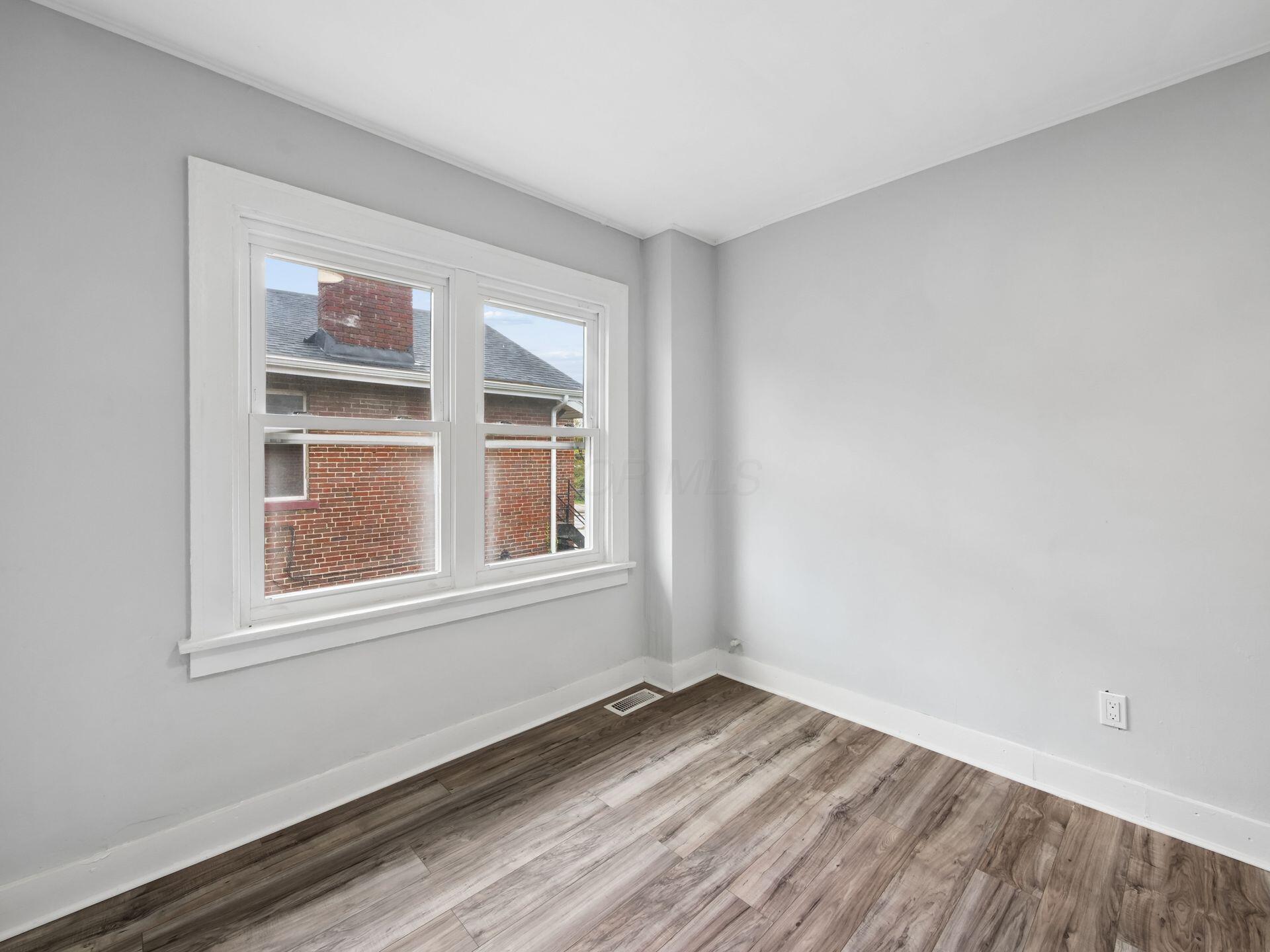 Empty room with wood-look flooring and a large window facing a neighboring brick building.