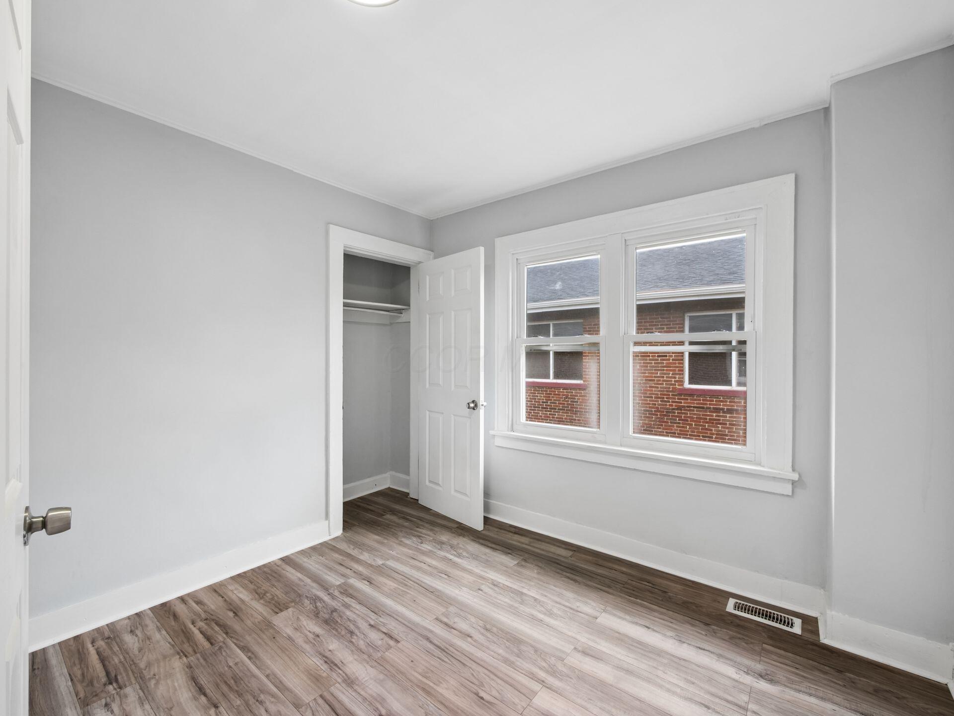 Empty bedroom with wood-look floors, an open closet, and a large double window.