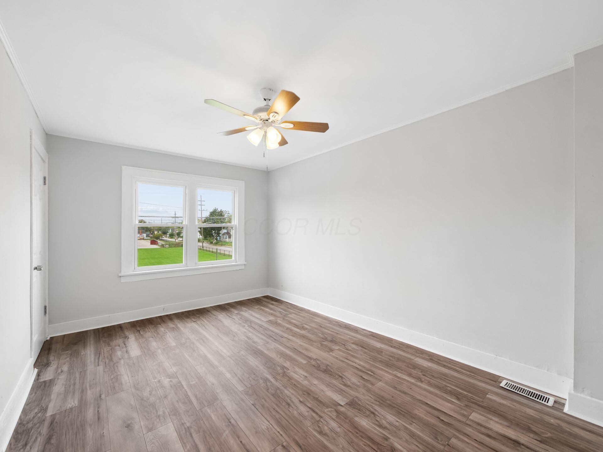 Empty room with wood-look floors, a ceiling fan, and a double window overlooking a green lawn.