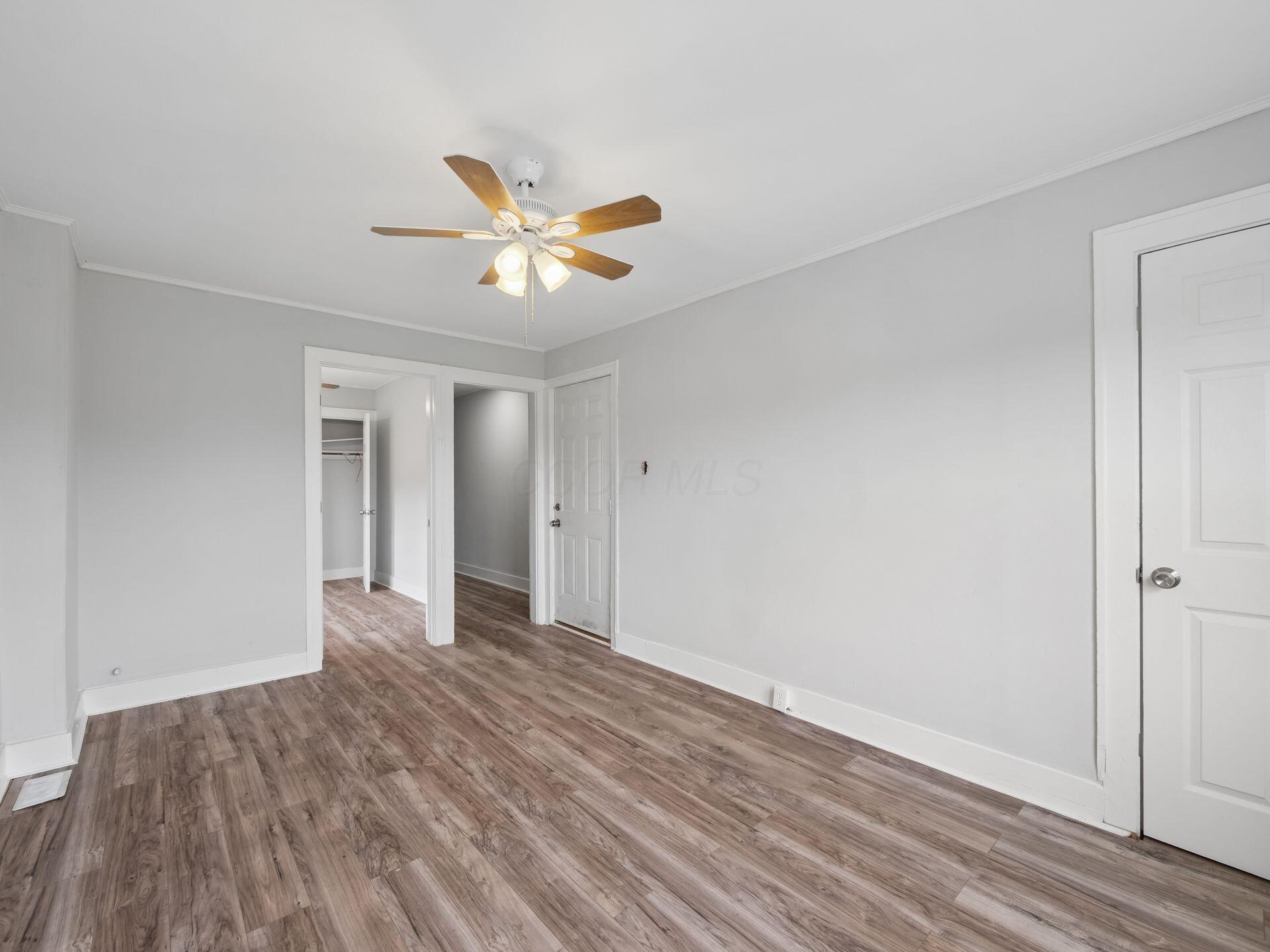 Empty room with wood-look flooring, a lit ceiling fan, and an open closet doorway.