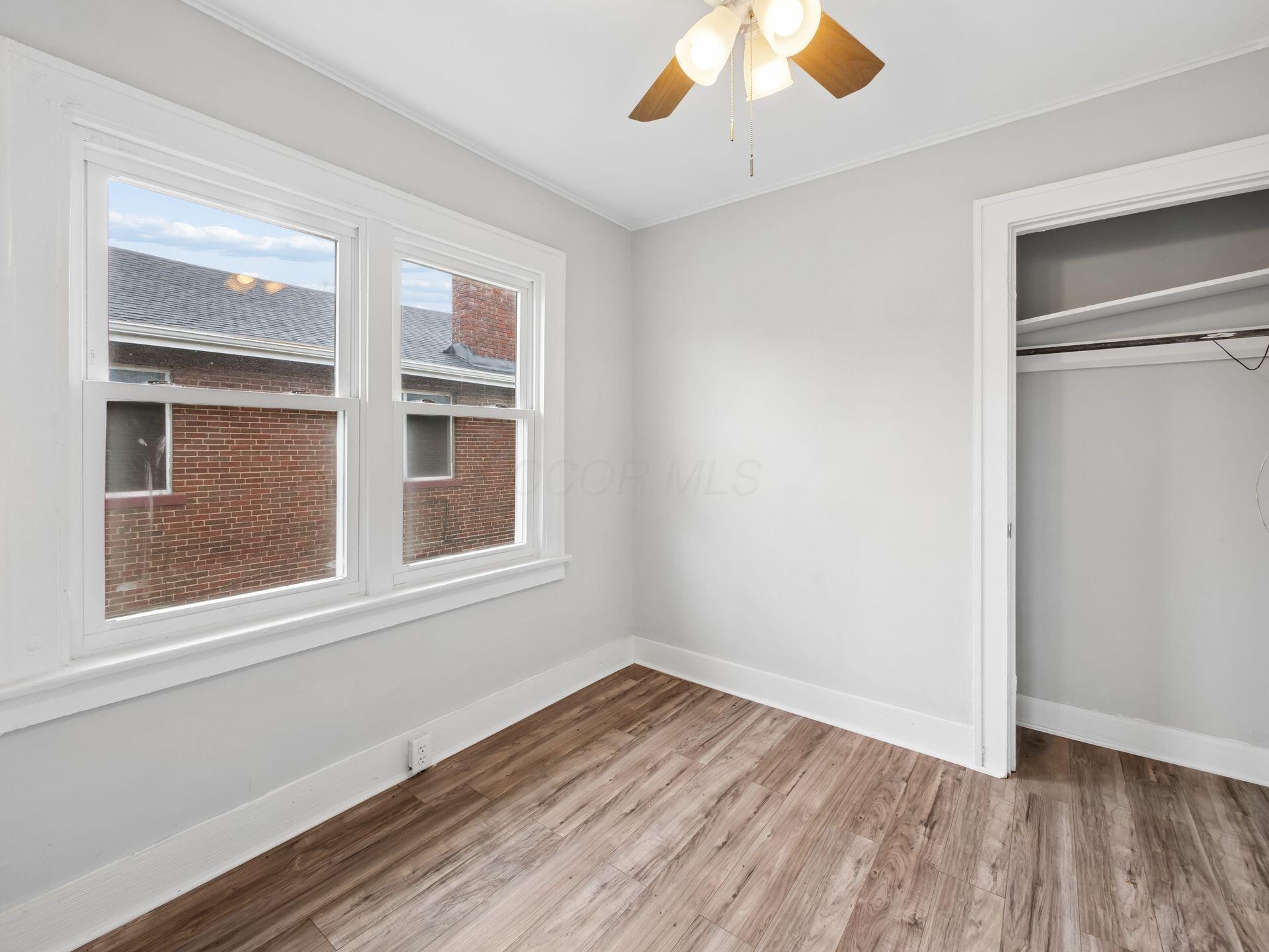 Empty bedroom with two windows, wood-look flooring, ceiling fan, and open closet.