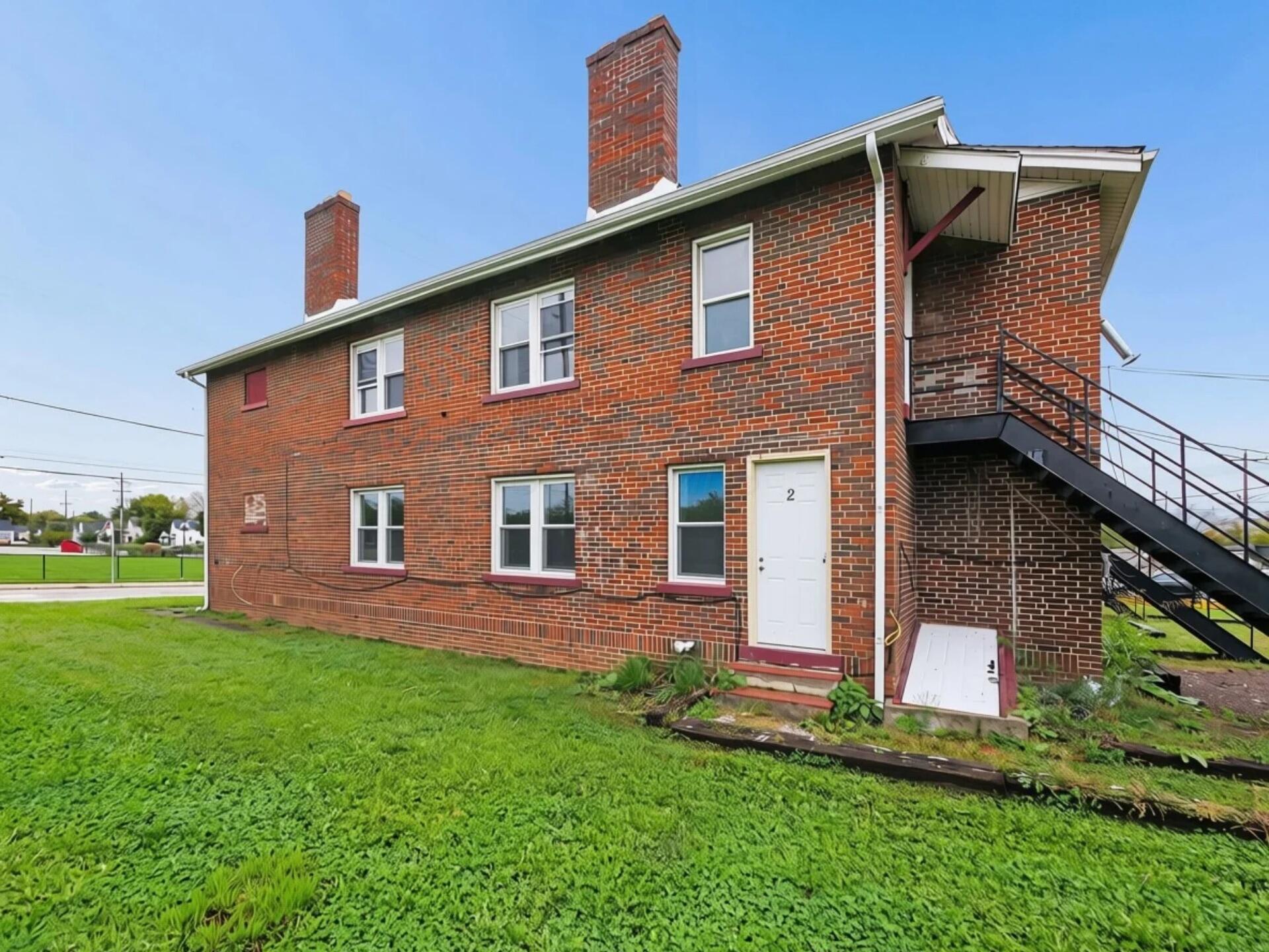 Two-story red brick building with white-trimmed windows, chimneys, and an exterior metal staircase.