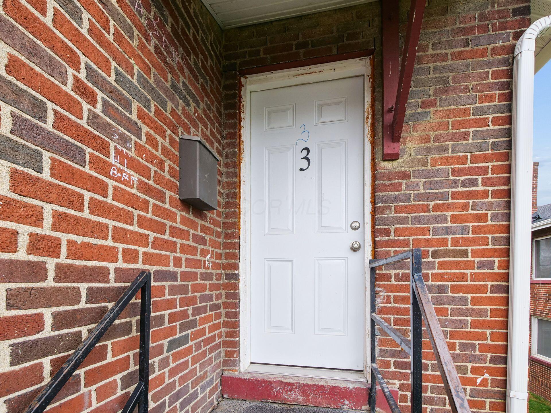 White door marked 3 in a brick entryway with a mailbox and metal railings.