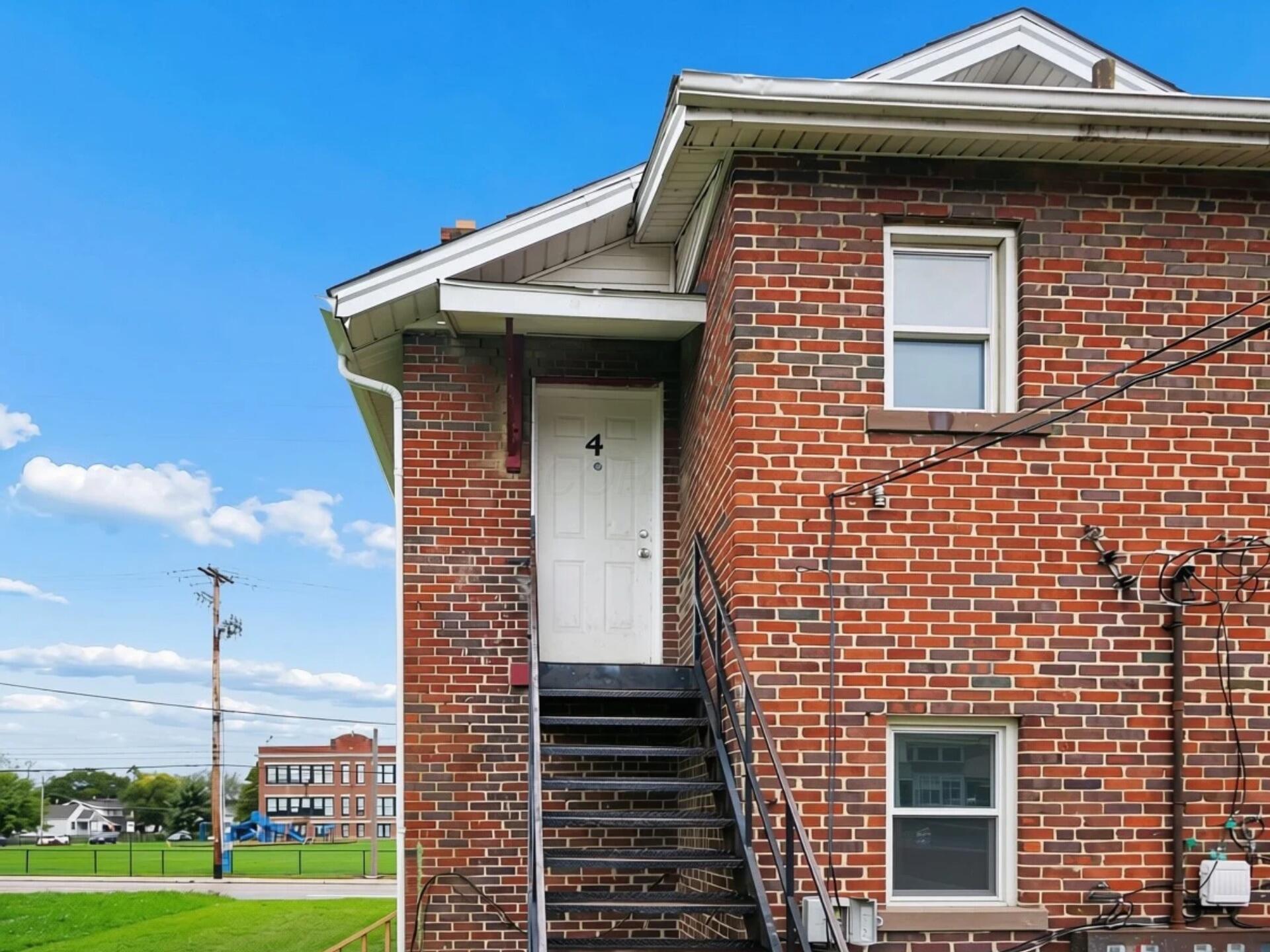 Brick multi-unit building with exterior stairs leading to an upper-level entrance.