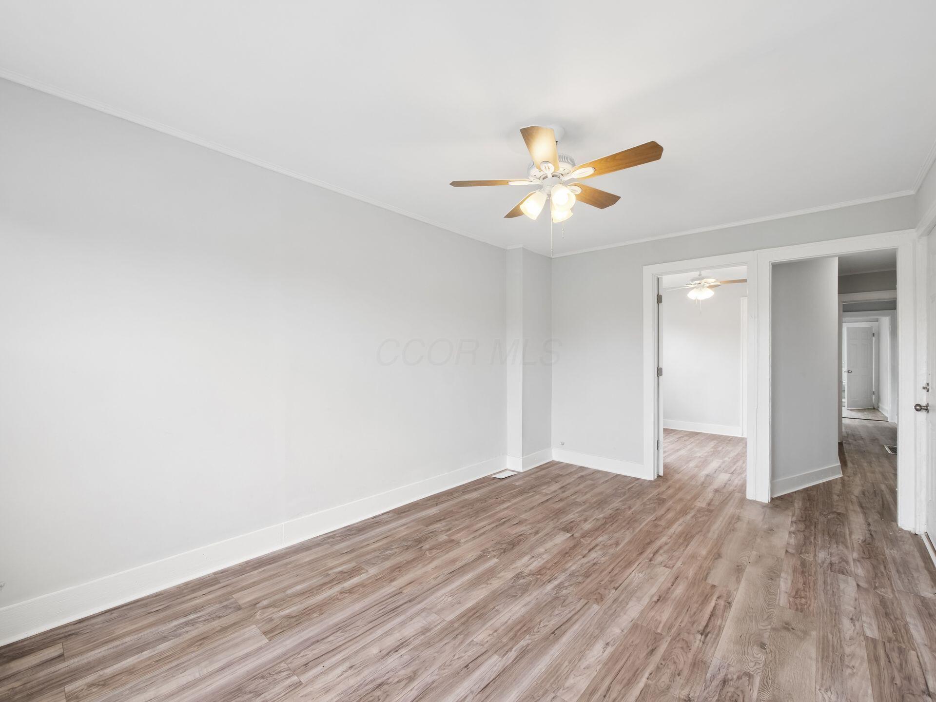 Empty room with wood-look flooring, a ceiling fan, and open doorways to adjoining spaces.