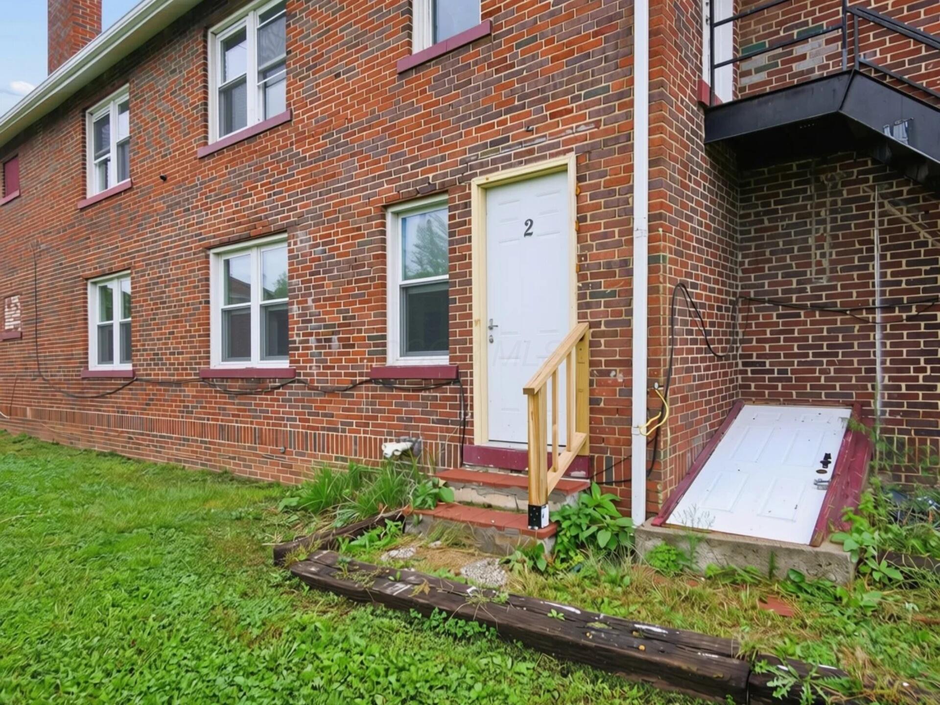 Red-brick building entrance with white door marked 2, wooden handrail, and basement hatch.