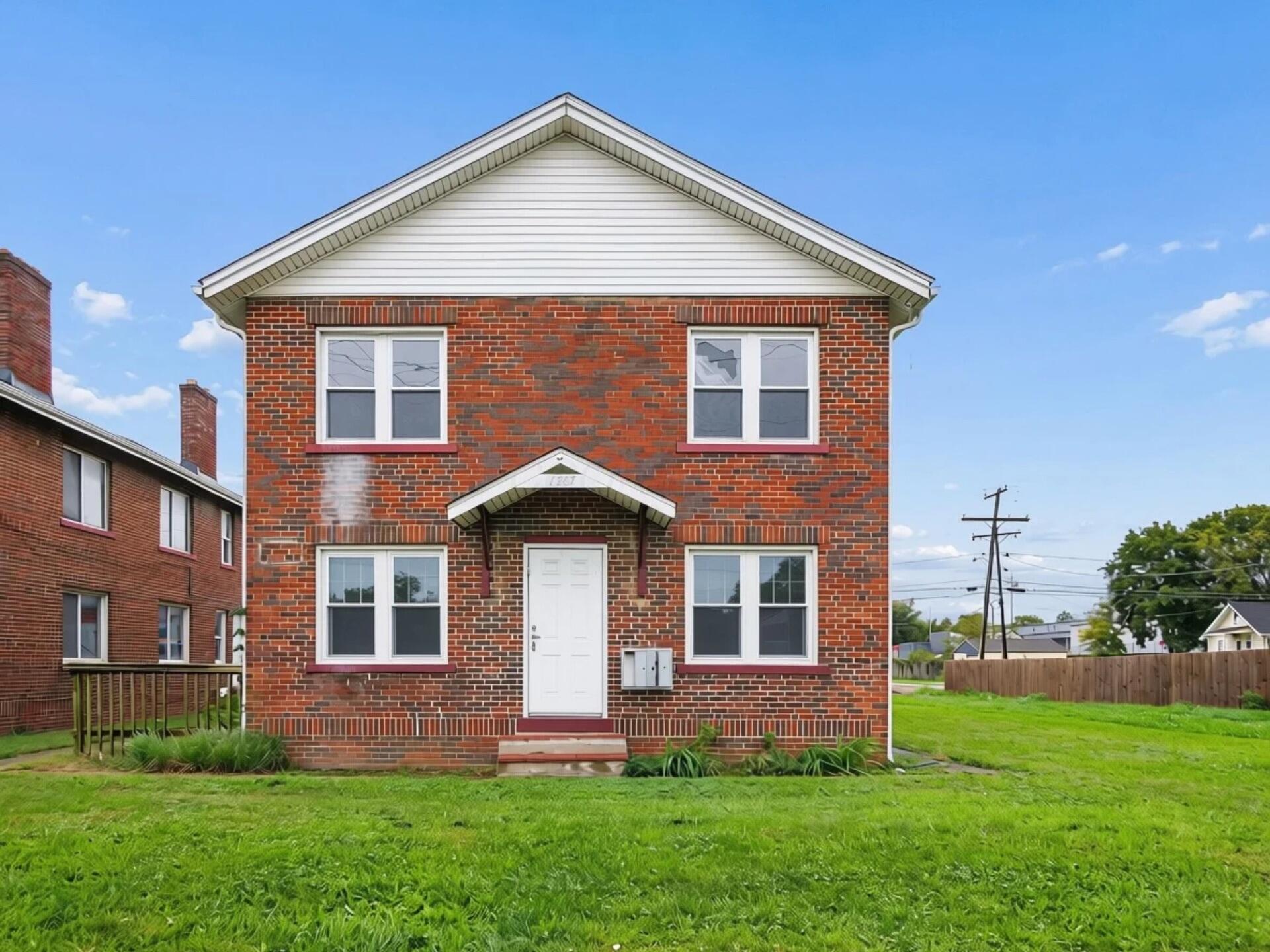 Two-story red brick building with a white gable, covered entrance, and broad green lawn.