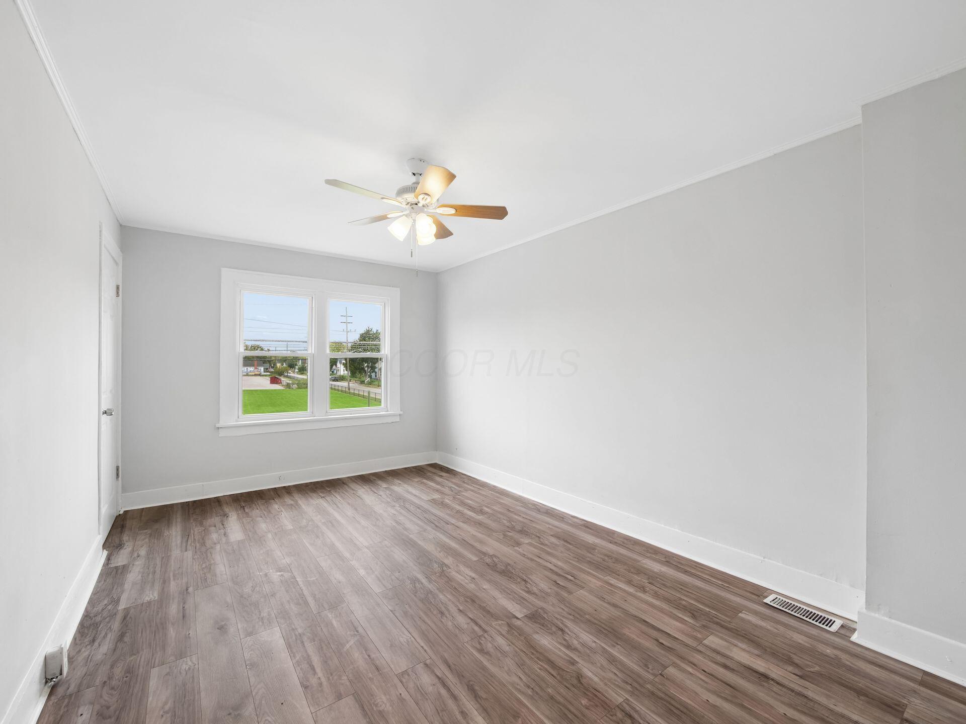 Empty room with wood-look flooring, a ceiling fan, and a double window.
