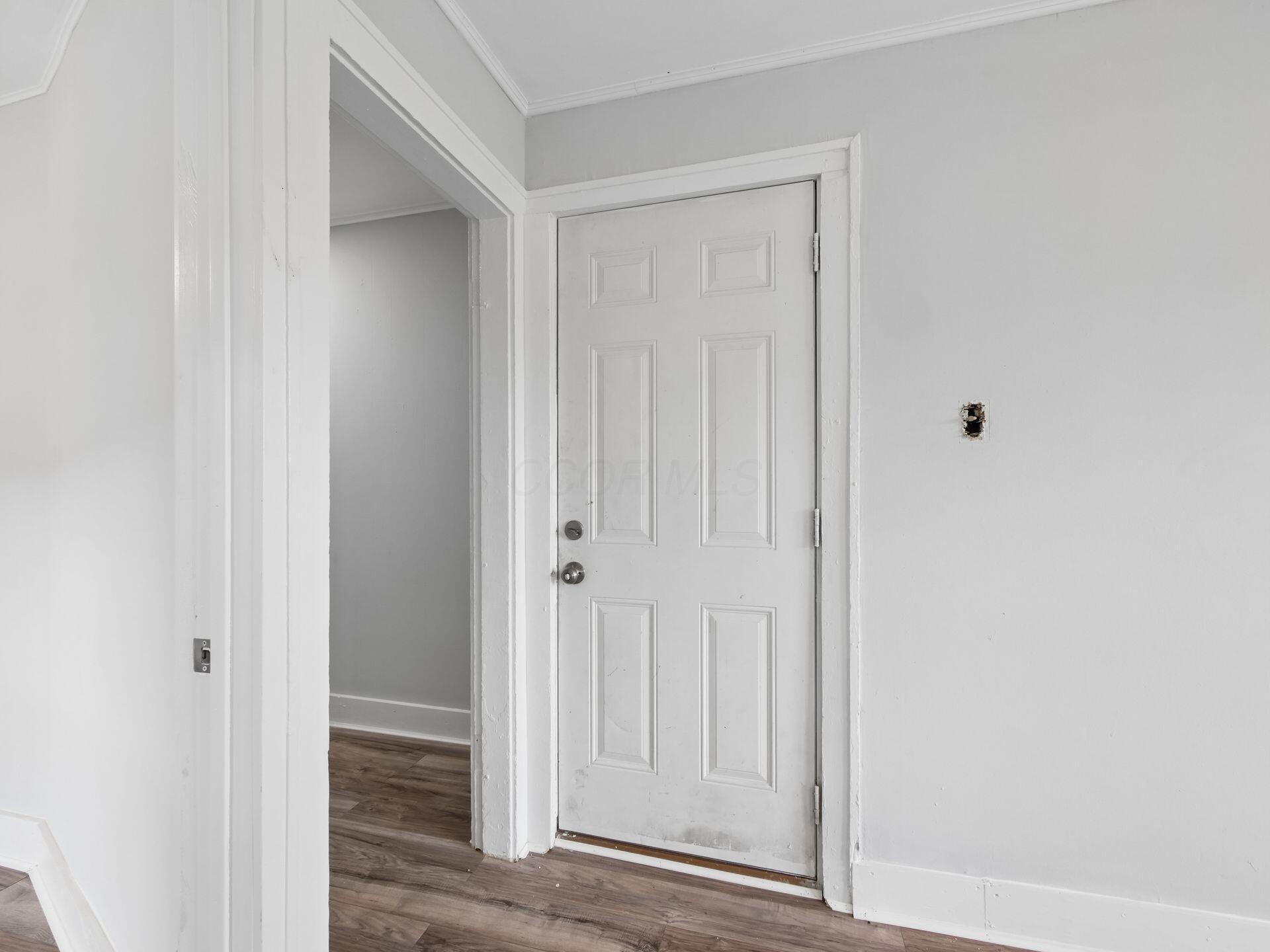 Entryway with a white paneled front door, wood-look flooring, and an open doorway to another room.