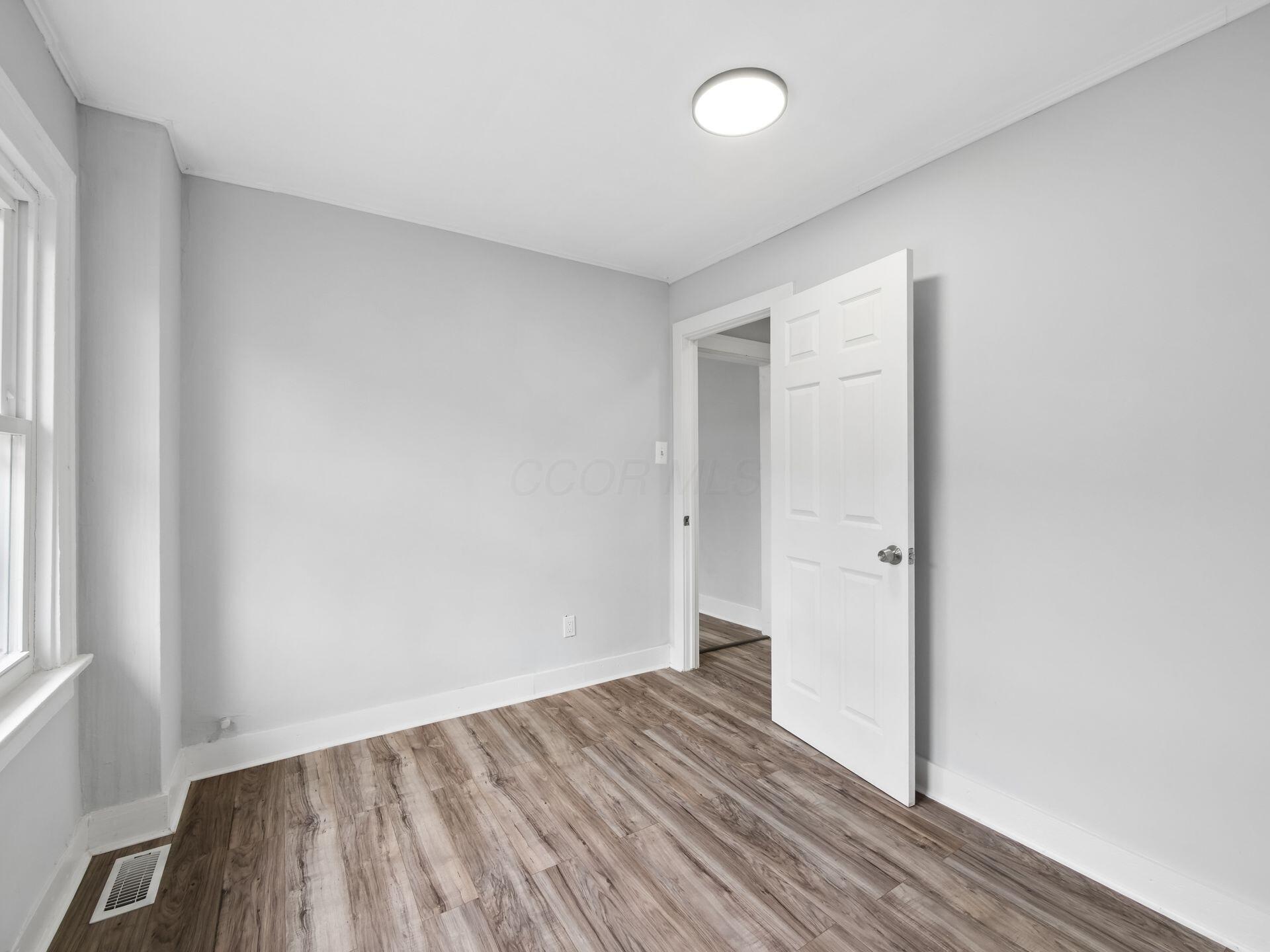 Empty room with gray walls, wood-look flooring, a window, and an open door.