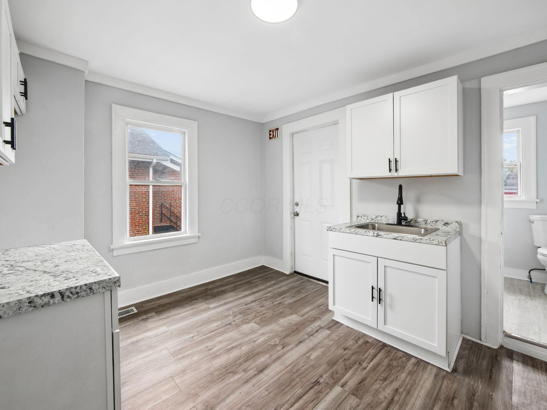 Vacant kitchen with white cabinets, a stainless steel sink, and wood-look flooring.